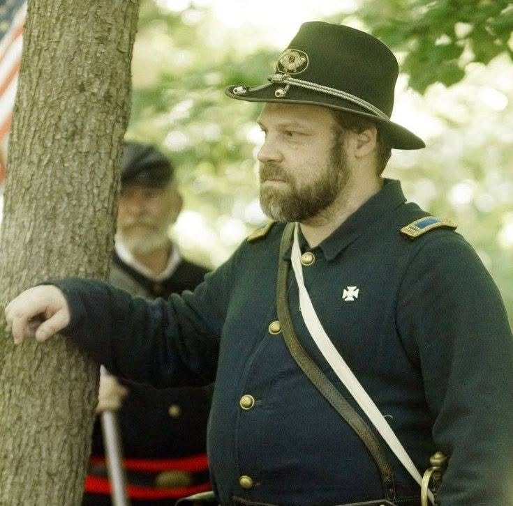 Sean Protas in Union uniform at a living history event, standing beside a tree in wooded ground