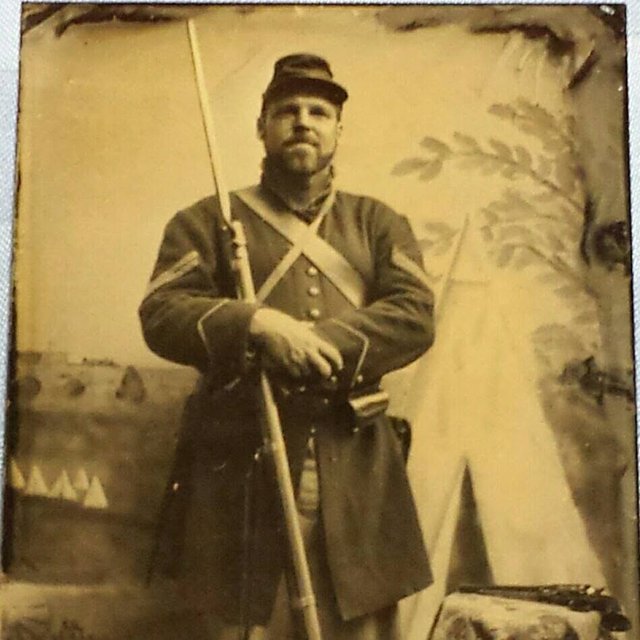 Wet-plate style portrait of a Union sergeant standing with his musket before a painted studio backdrop